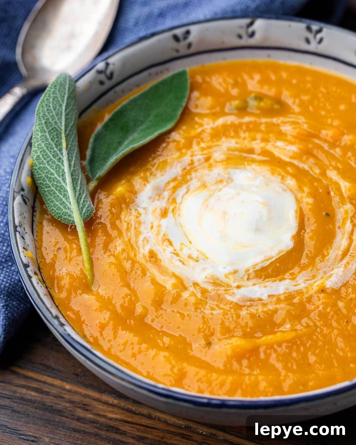 Roasted butternut squash soup in white and blue bowl with sage leaf garnish.