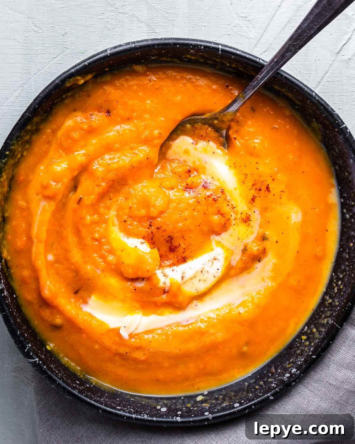 Butternut squash soup in black bowl topped with cream and nutmeg.
