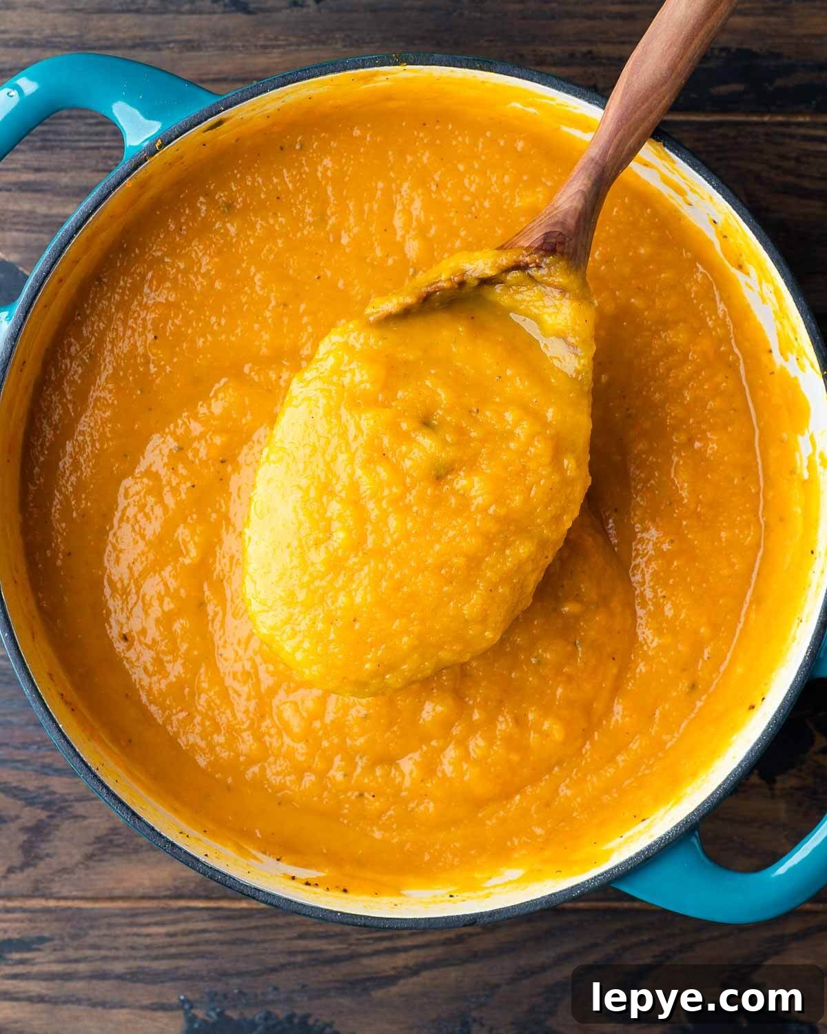 Large spoon scooping out butternut squash soup from Dutch oven pot.