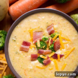 Loaded Broccoli Cheese & Potato Soup in a dark colored bowl with carrots and broccoli in the background