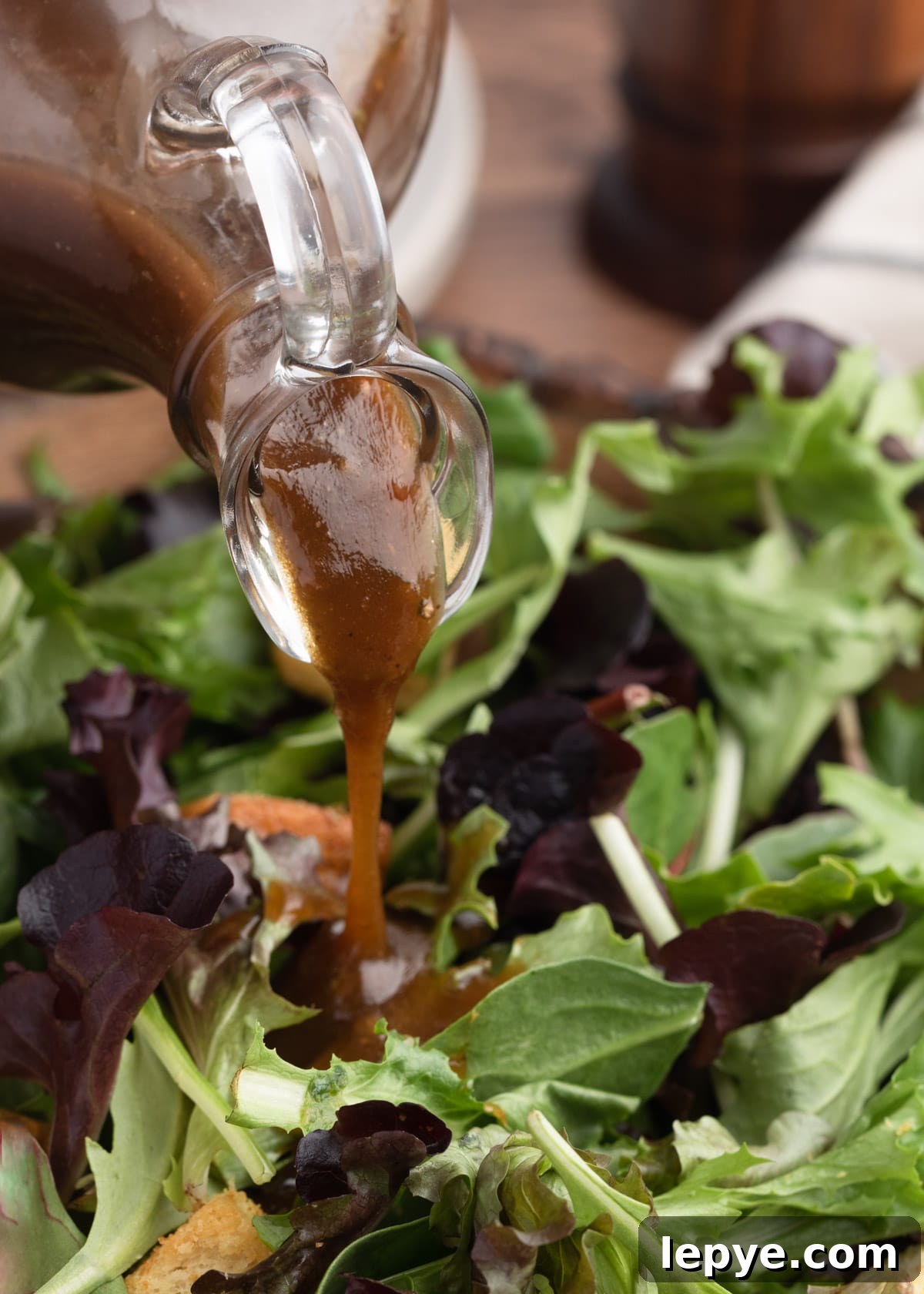 Classic Balsamic Vinaigrette Dressing Recipe 5 closeup of balsamic vinaigrette being poured from a glass cruet over spring mix greens