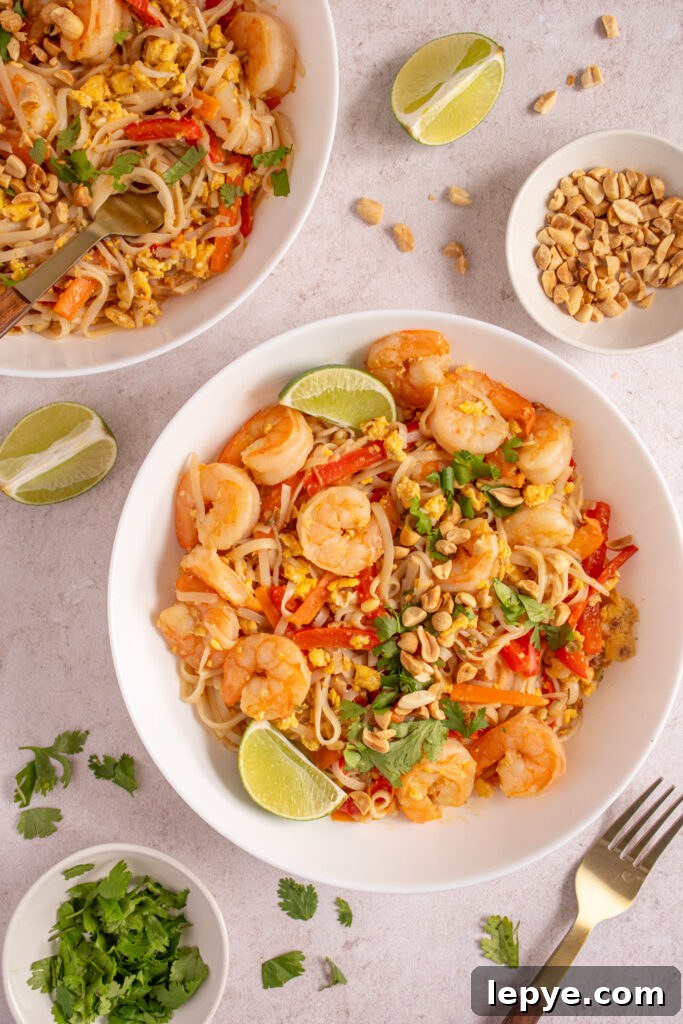 Overhead view of white bowls filled with shrimp pad thai and garnished with cilantro and chopped peanuts.