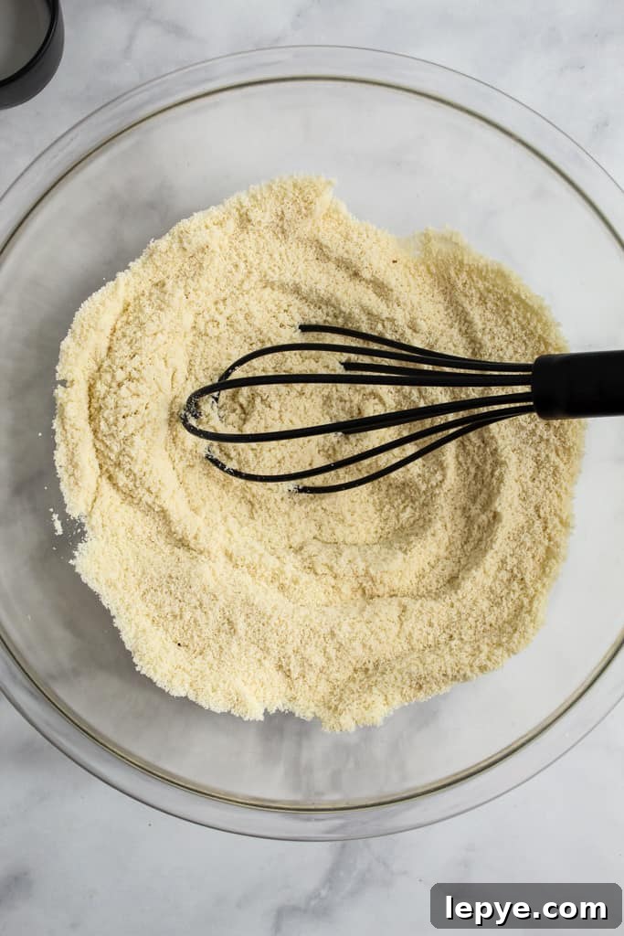 flours in a glass bowl with a black whisk