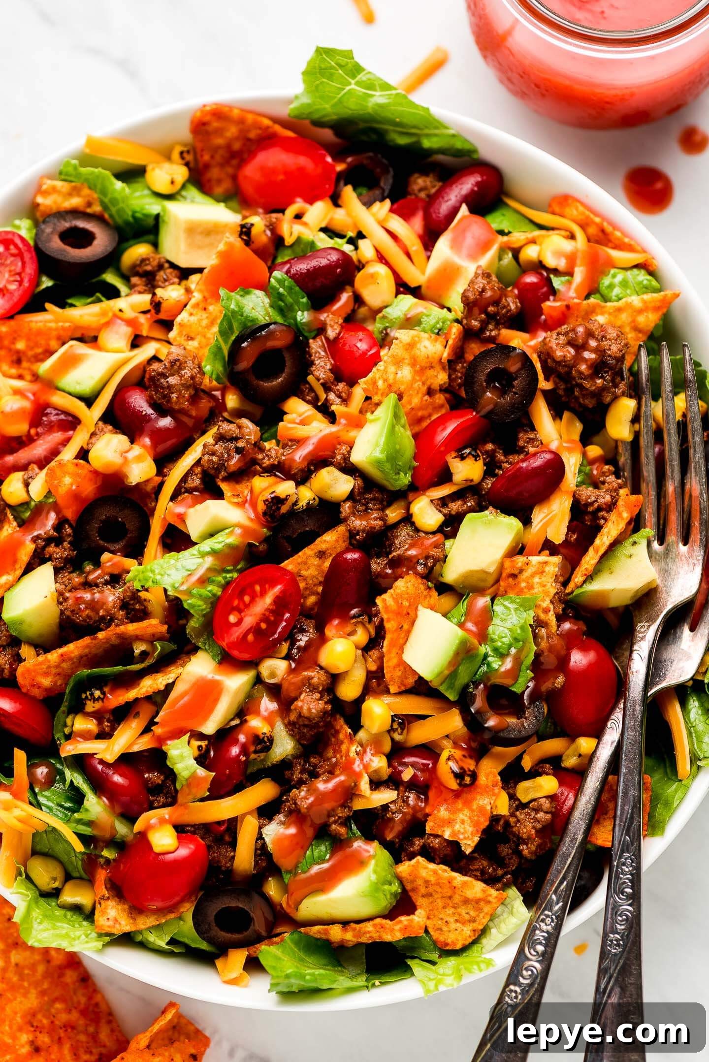 Dorito Taco Salad Recipe: Crunchy Tex-Mex Dinner Idea 2 Close up shot of Dorito Taco Salad drizzled with Catalina dressing and two forks in the side.
