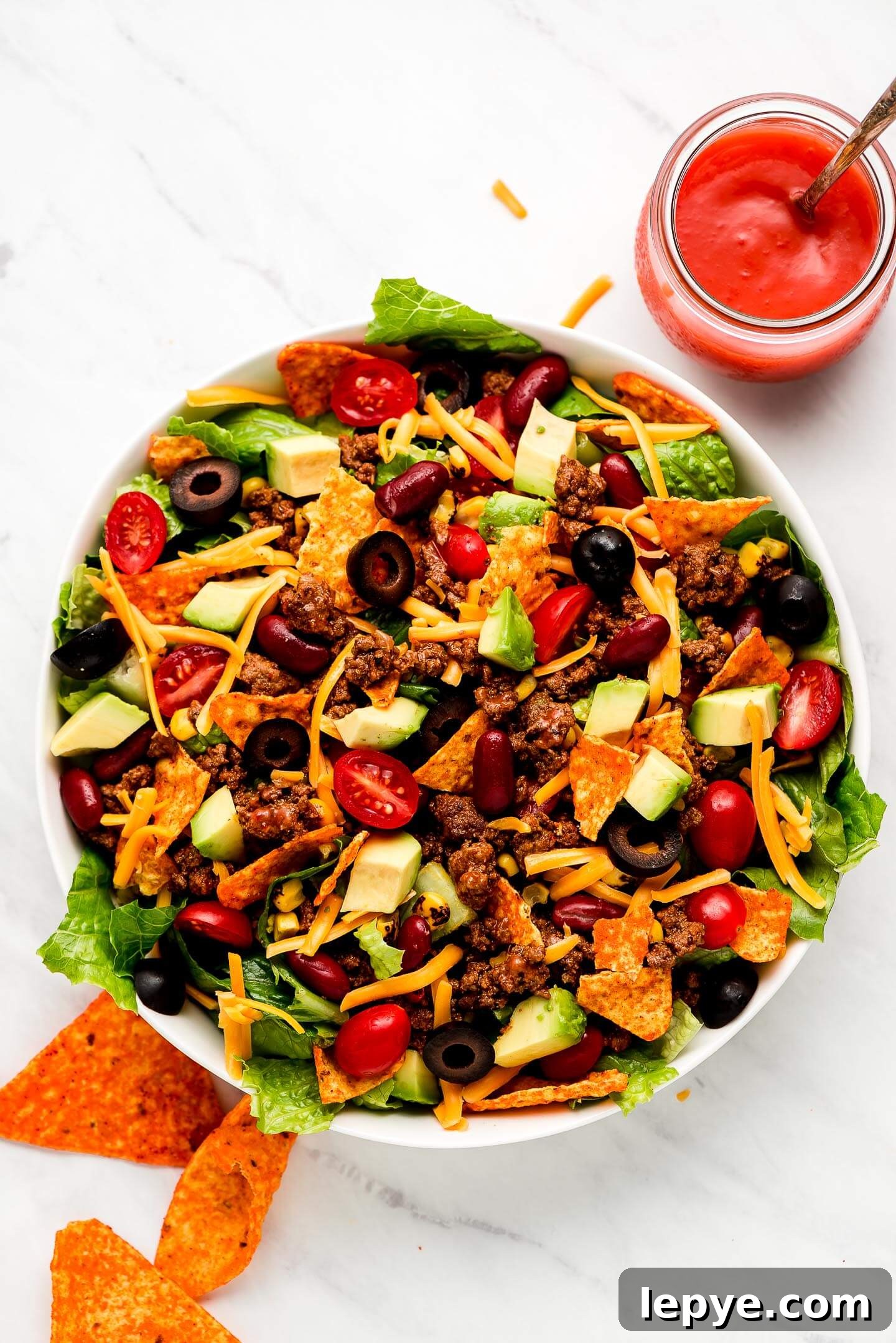 Dorito Taco Salad Recipe: Crunchy Tex-Mex Dinner Idea 3 A large bowl full of Dorito Taco Salad with a jar of Catalina dressing to the side.