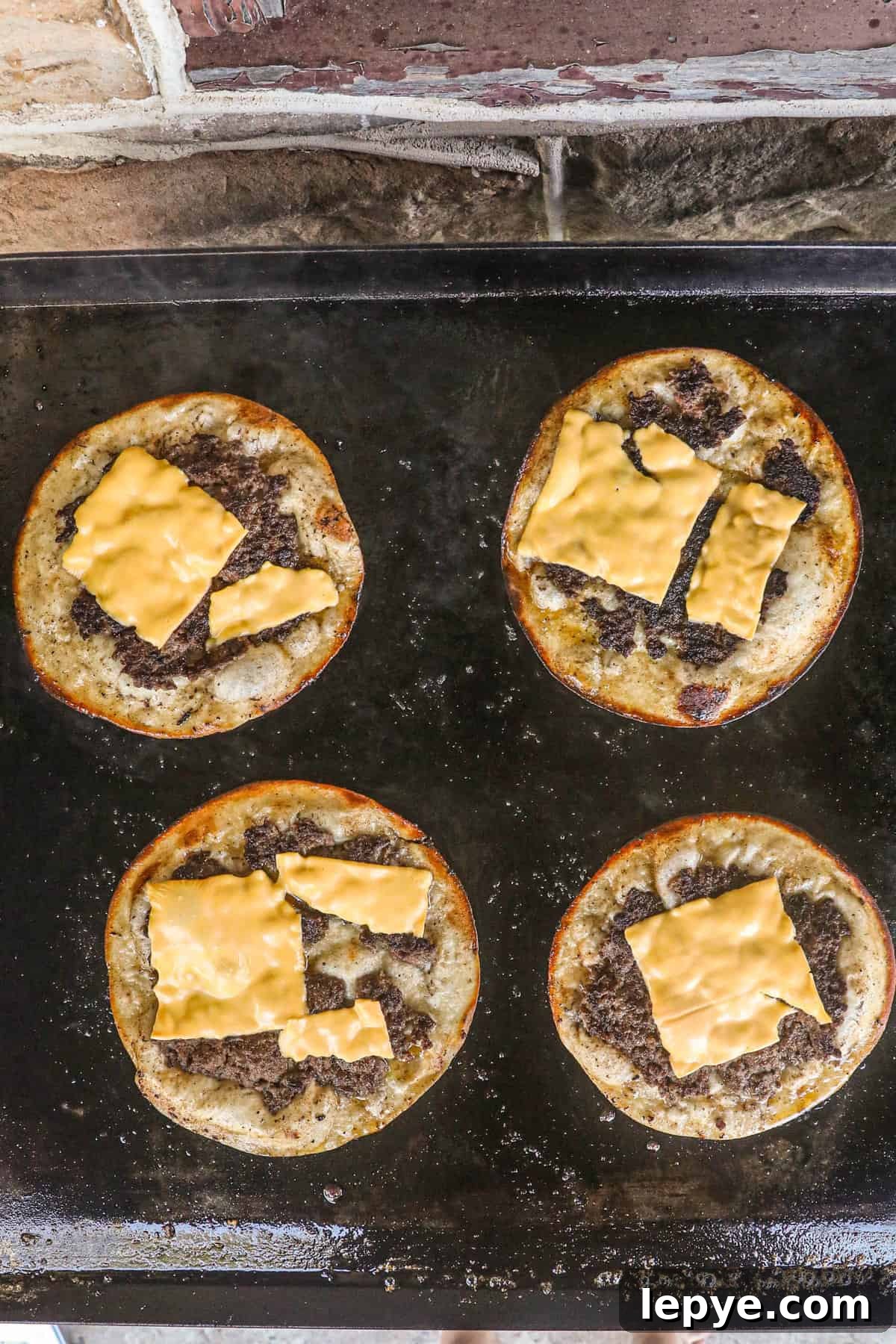 Adding cheese to Smash Burger Tacos on Blackstone