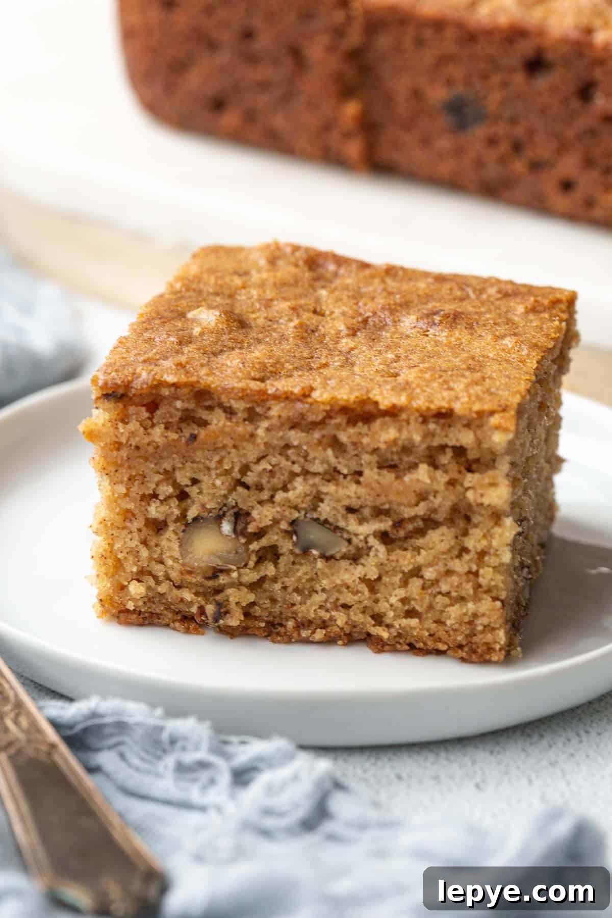 slice of applesauce cake on a white plate next to a fork.