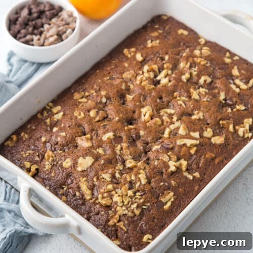 old fashioned date cake topped with walnuts in a white casserole dish.