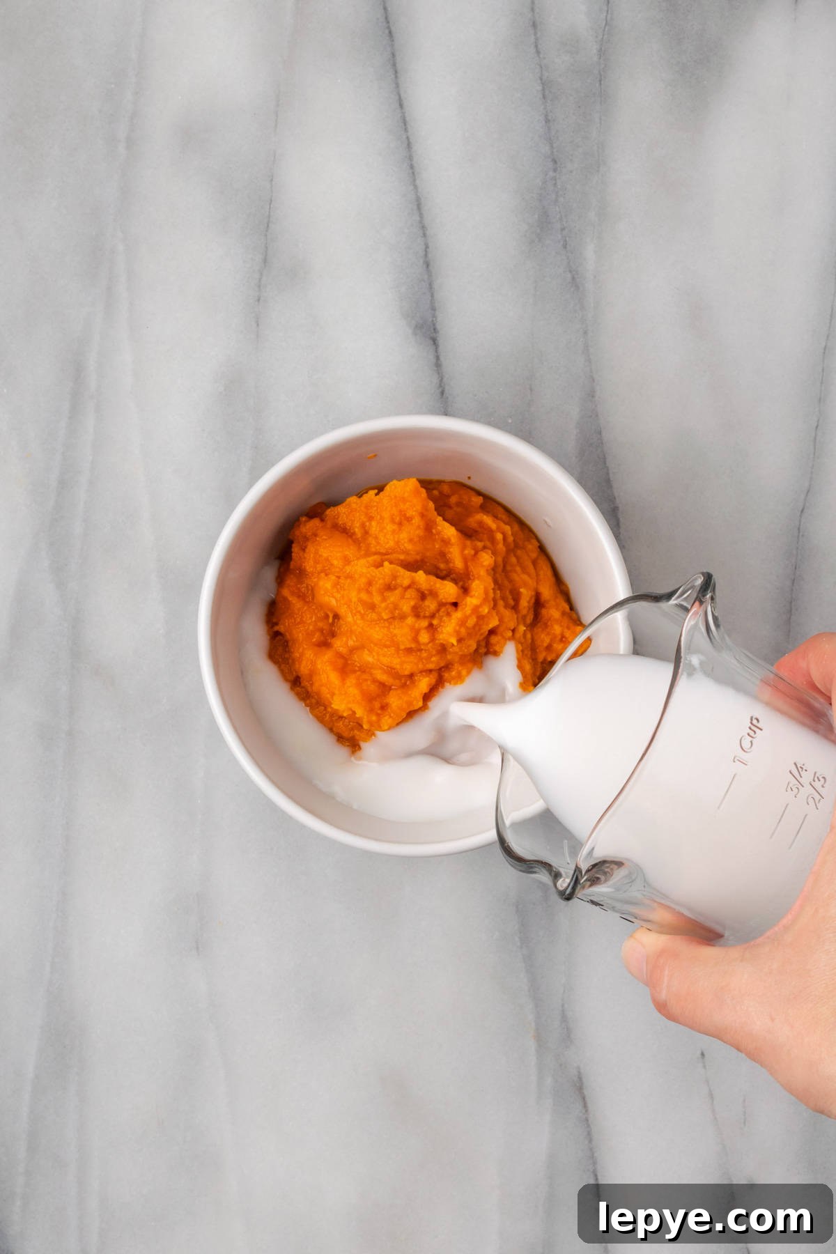 Milk being poured into a bowl of pumpkin puree.
