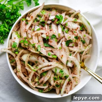 sliced onions in a white bowl with sumac seasoning and parsley.