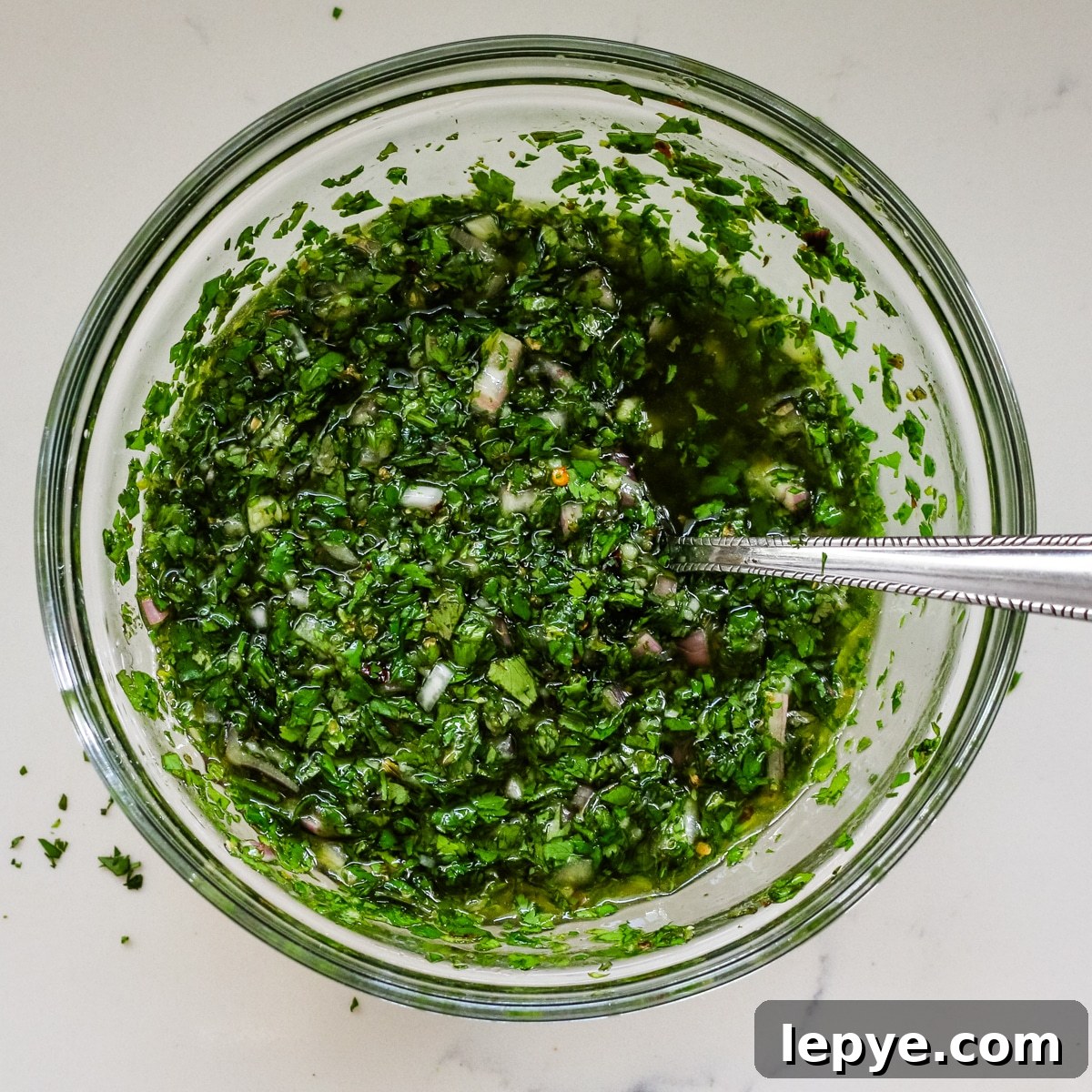 Cilantro Chimichurri Sauce Recipe — Fresh Herb Marinade for Grilled Meats 7 cilantro chimichurri sauce mixed in glass bowl with spoon.