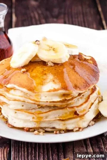 A stack of banana pancakes topped with sliced banana and maple syrup.
