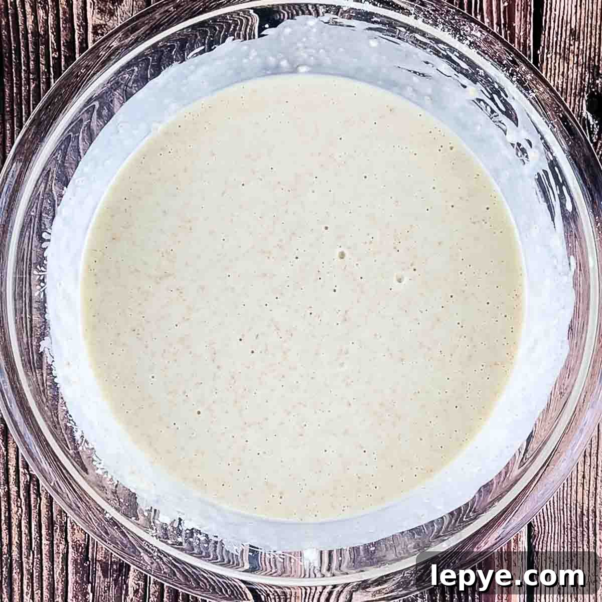 The waffle batter all mixed up in a glass mixing bowl.