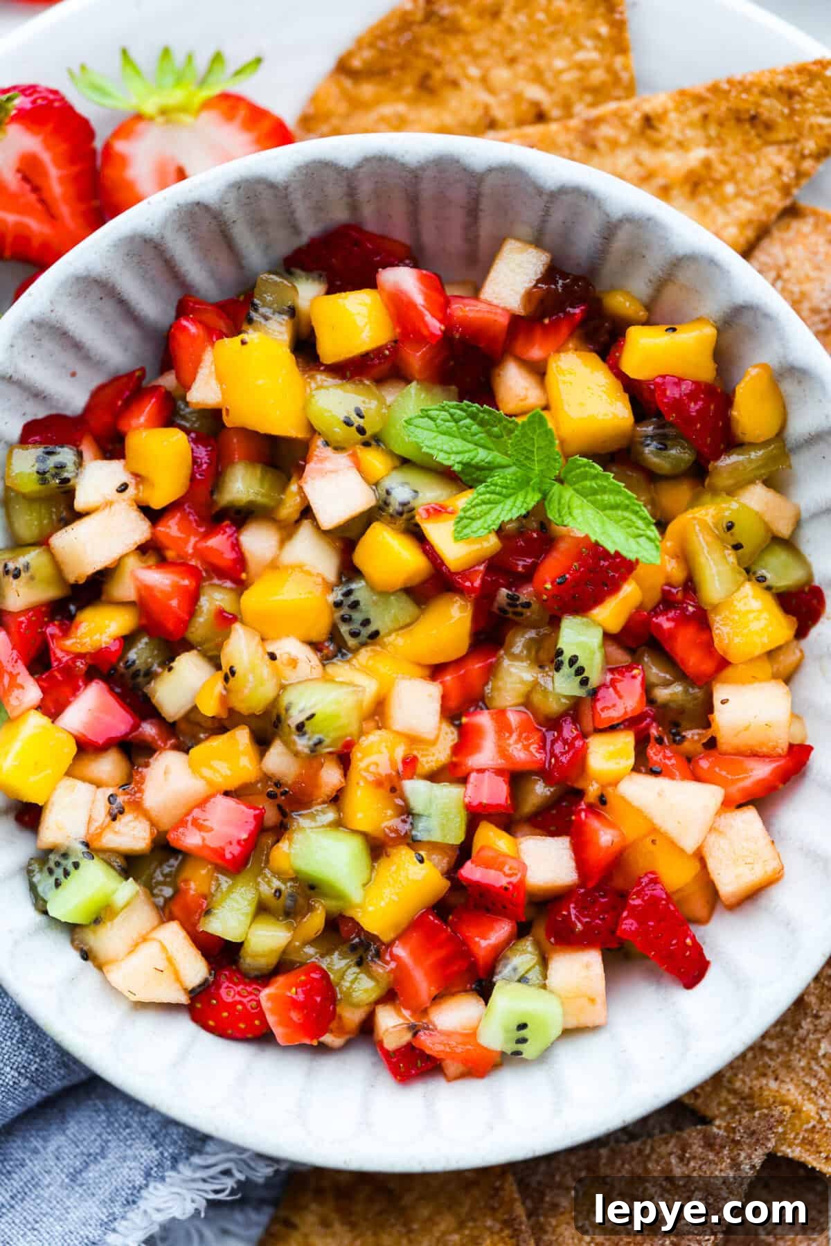 Vibrant fruit salsa is a fresh, juicy twist on your favorite snack! Sweet berries, tropical mango, and a splash of lime always steal the spotlight! Especially when served with crispy cinnamon chips! Close up shot of a bowl of fresh fruit salsa.
