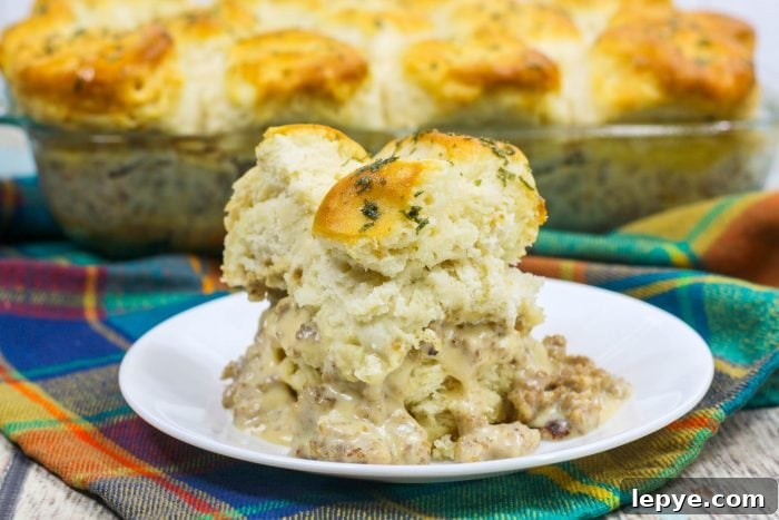 a white plate with layers of biscuits and sausage gravy on a rainbow tea towel. 