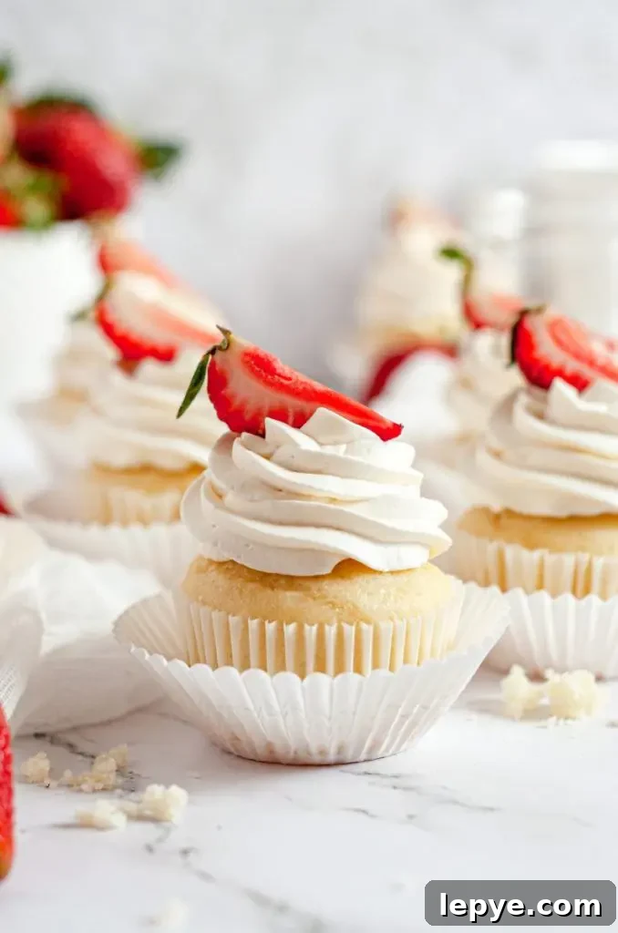 Lemon Raspberry Cupcakes with Gluten-Free & Dairy-Free Option 8 A close up picture of a strawberry shortcake cupcake. It is topped with a swirl of white whipped cream with a bright red strawberry slice on top.
