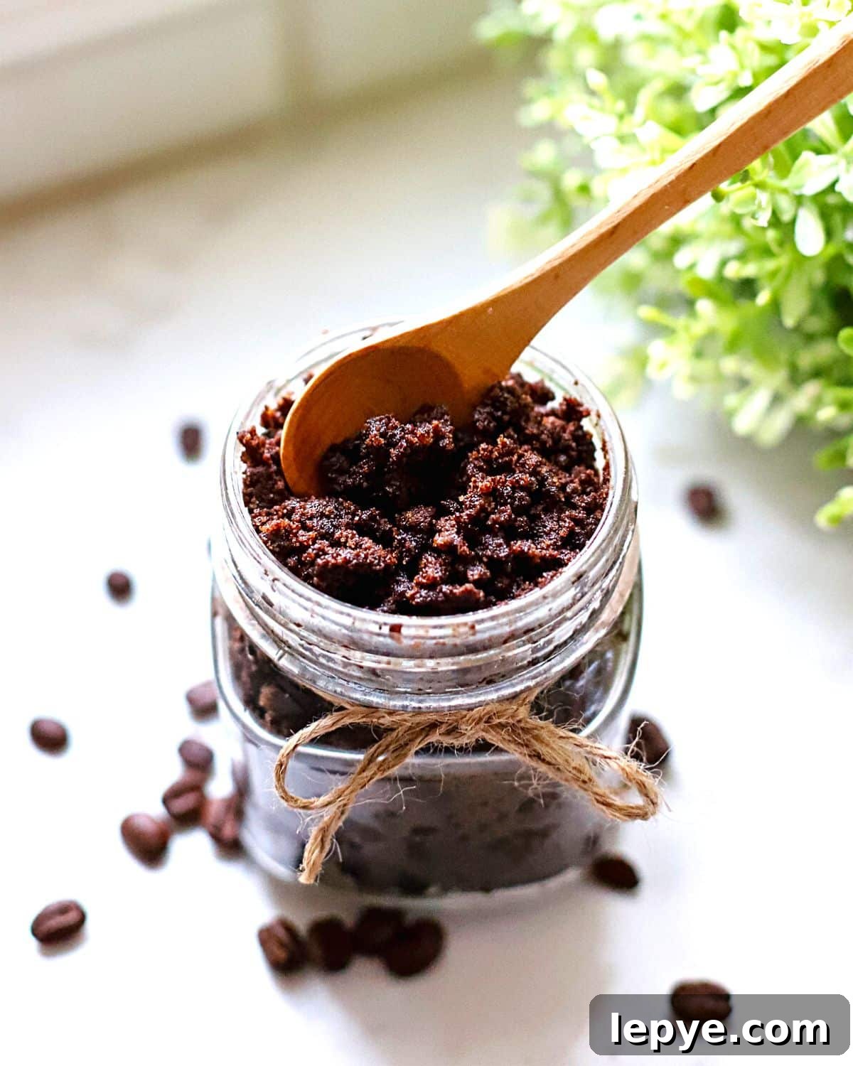 A coffee sugar scrub in a glass jar with a spoon sticking out of it.