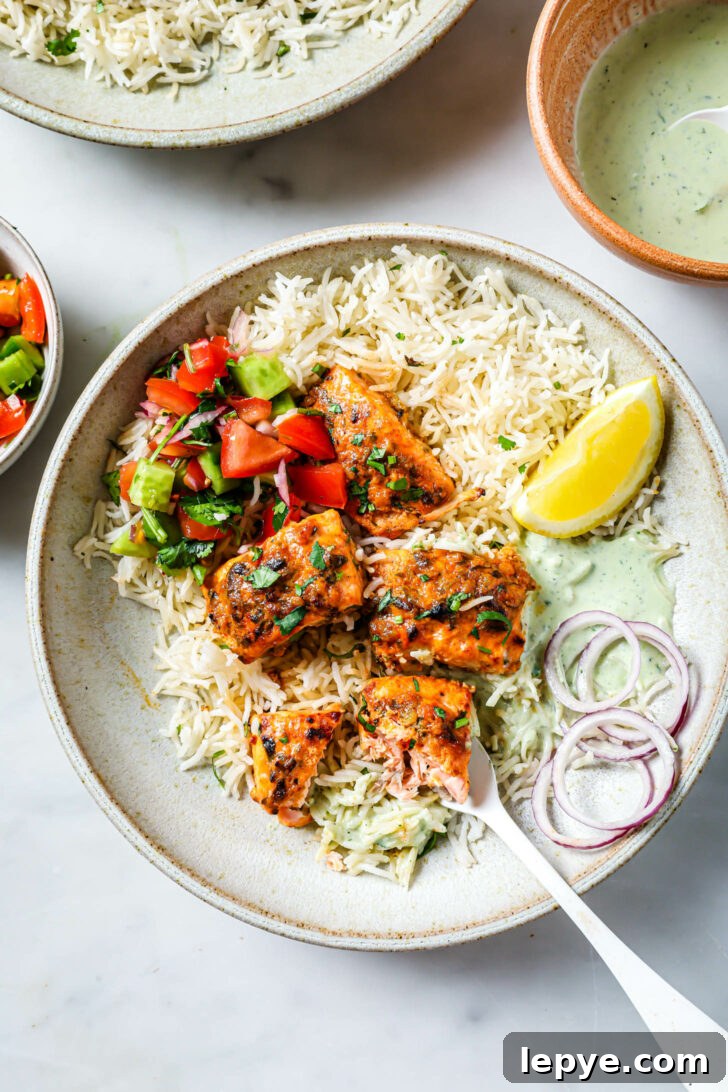 25-Minute Salmon Tikka Recipe: Quick Spiced Fish Tikka 2 Top view of a partially eaten plate of Salmon Tikka with rice, vegetables, onion and lemon.