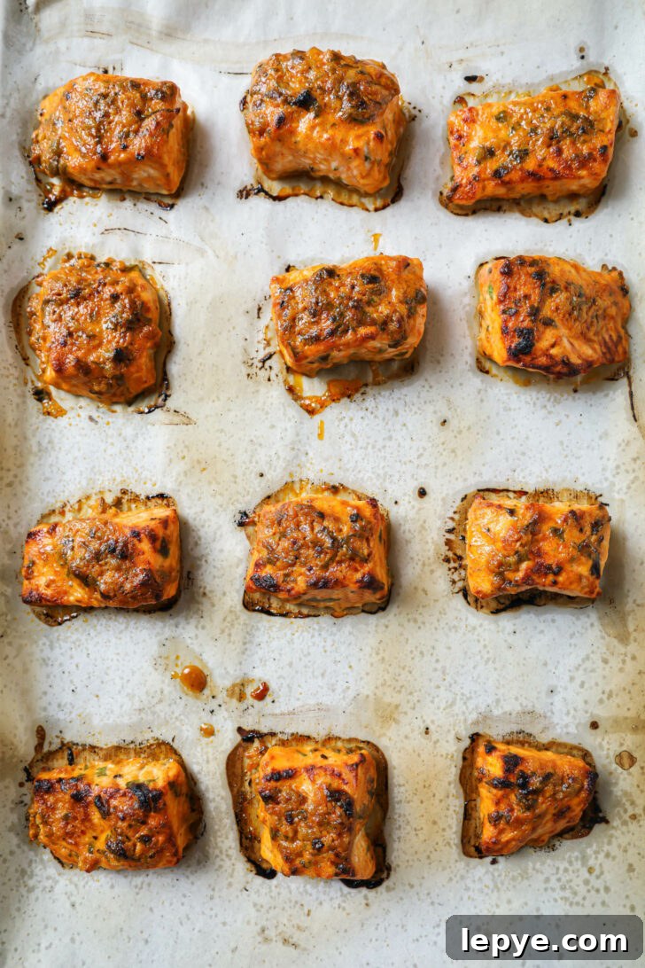 25-Minute Salmon Tikka Recipe: Quick Spiced Fish Tikka 9 Close up of a parchment covered sheet pan with baked Salmon Tikka sprinkled with parsley.