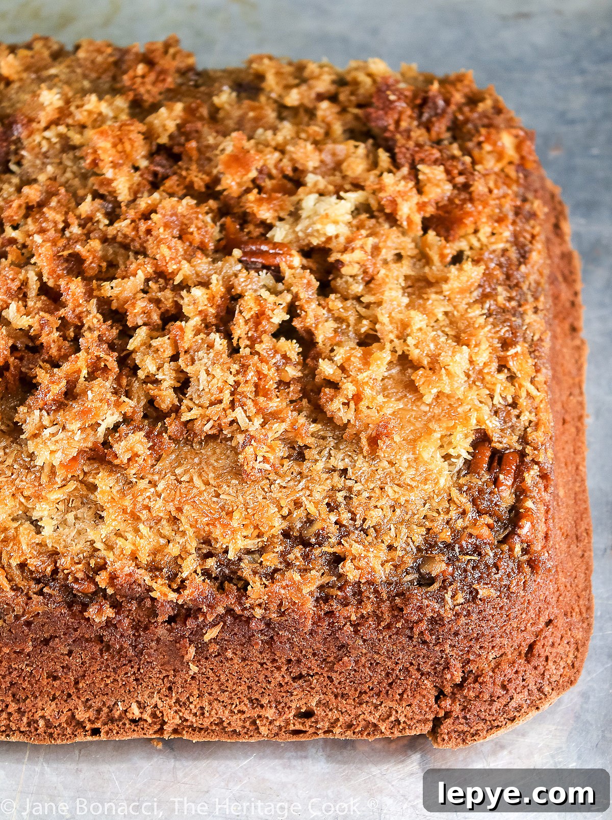 Square piece of cake with coconut/pecan frosting on a white plate; Cockeyed German Chocolate Cake © 2023 Jane Bonacci, The Heritage Cook.