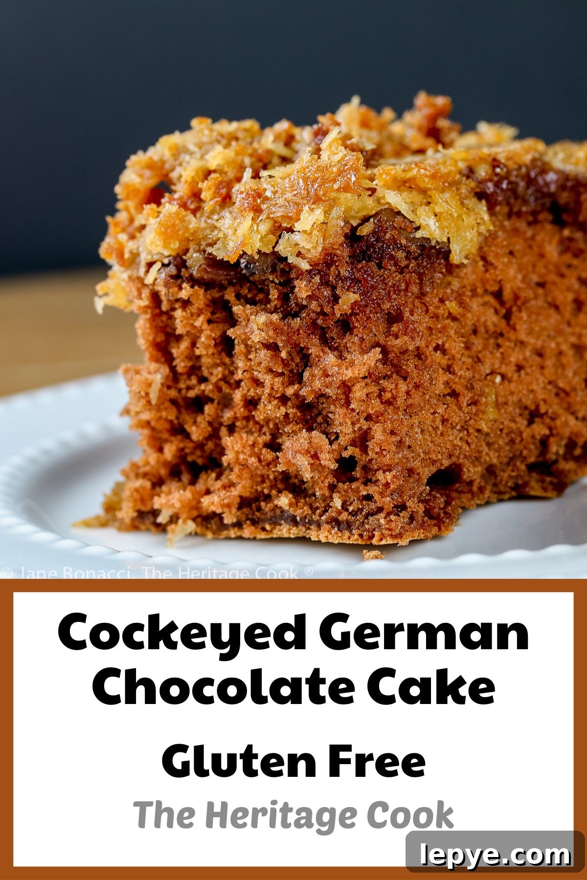Square piece of cake with coconut/pecan frosting on a white plate; Cockeyed German Chocolate Cake © 2023 Jane Bonacci, The Heritage Cook.