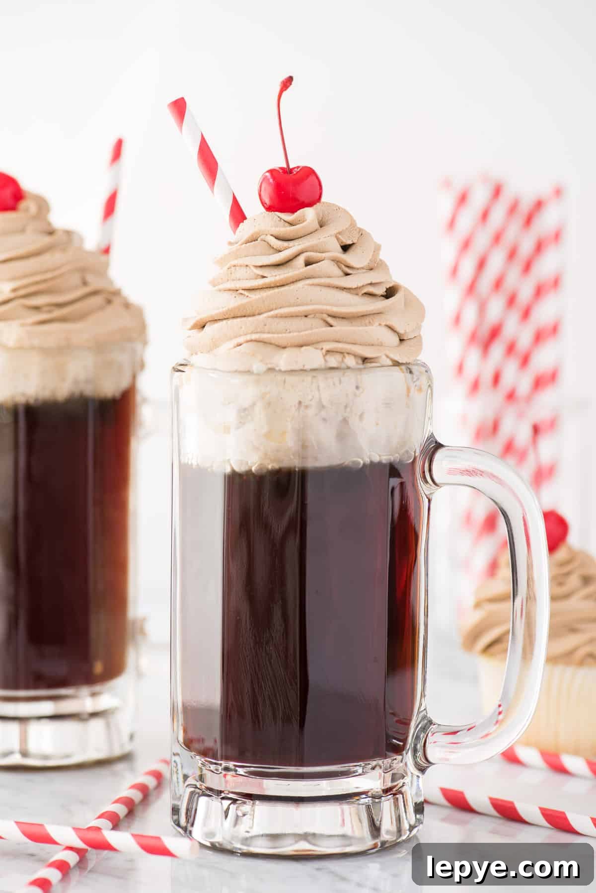 root beer whipped cream piped on top of root beer in a mug with maraschino cherry and red straw