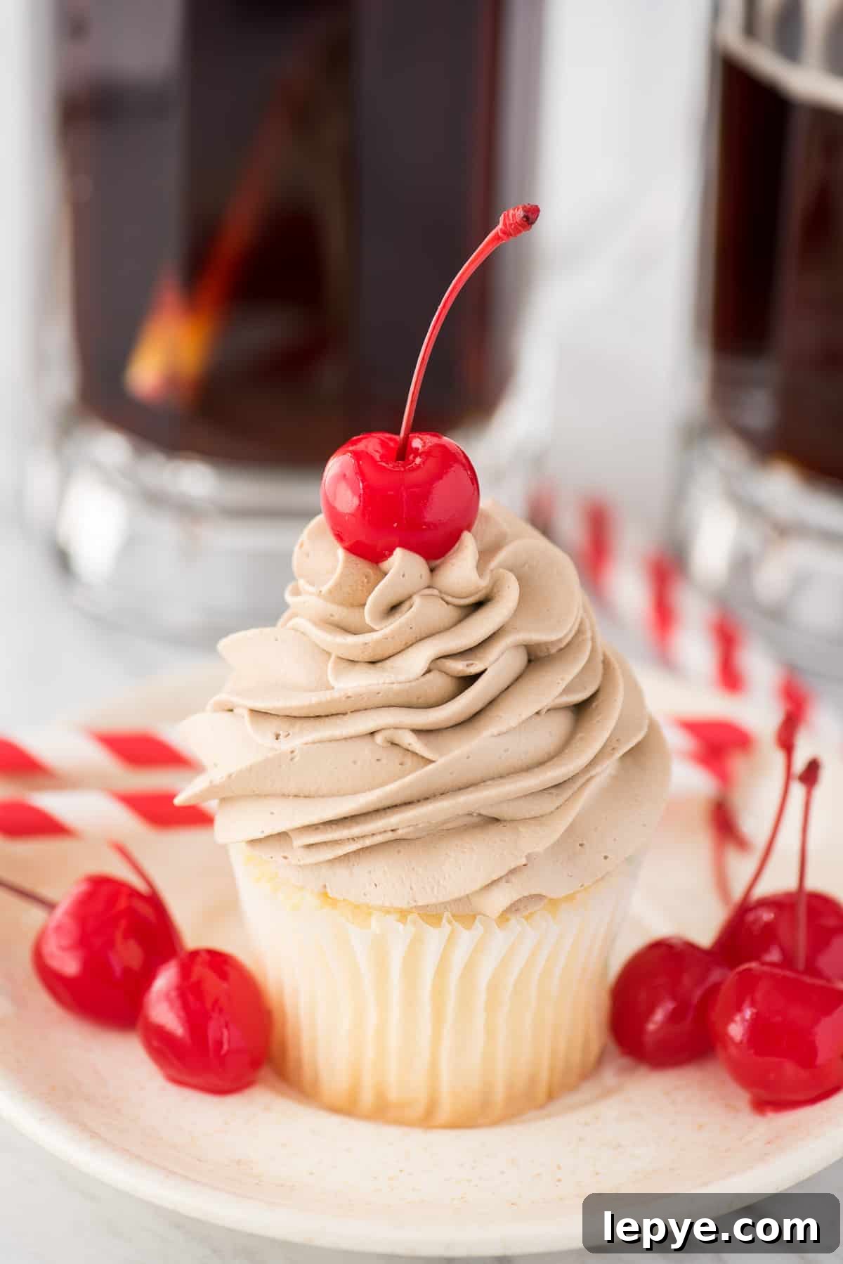 root beer whipped cream on top of white cupcake with maraschino cherry on white plate