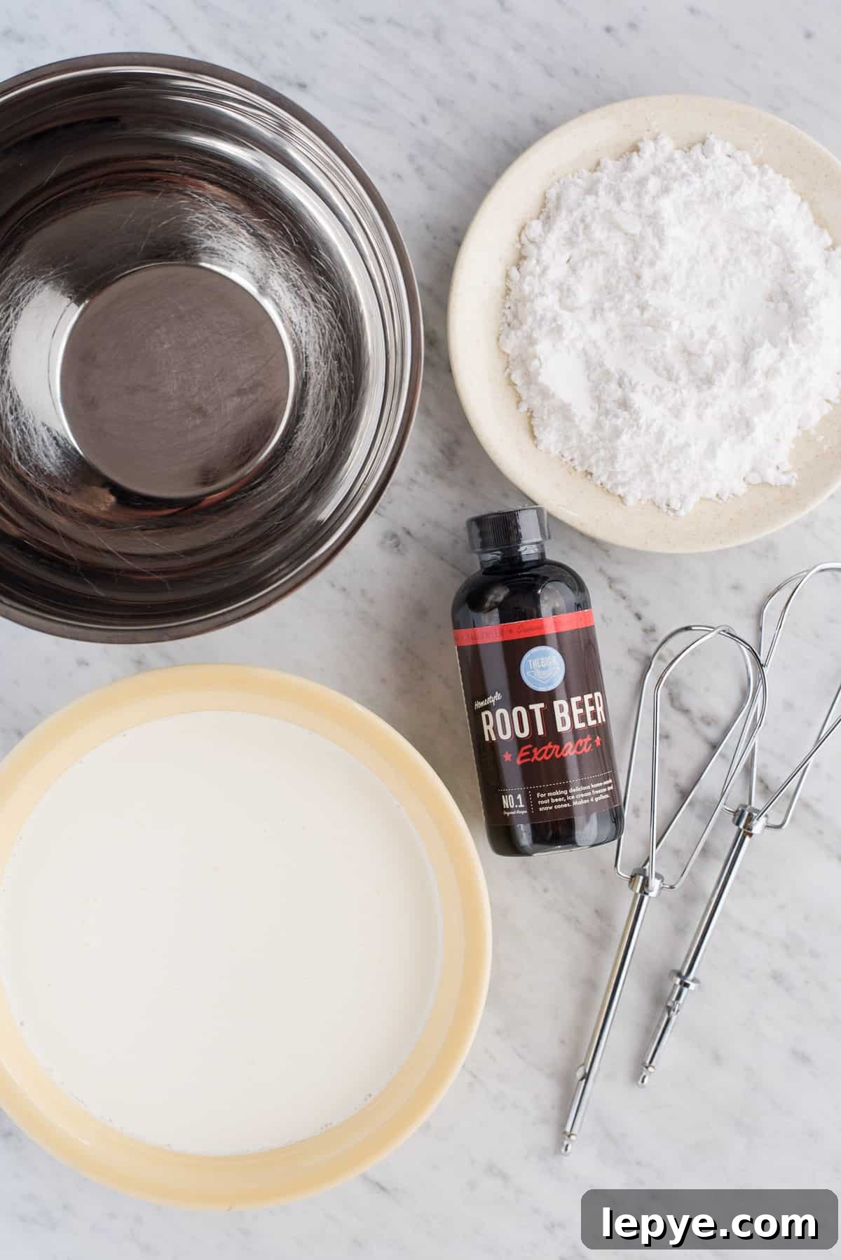 ingredients to make root beer frosting, includes metal bowl, powdered sugar, heavy cream, root beer extract and mixing beaters