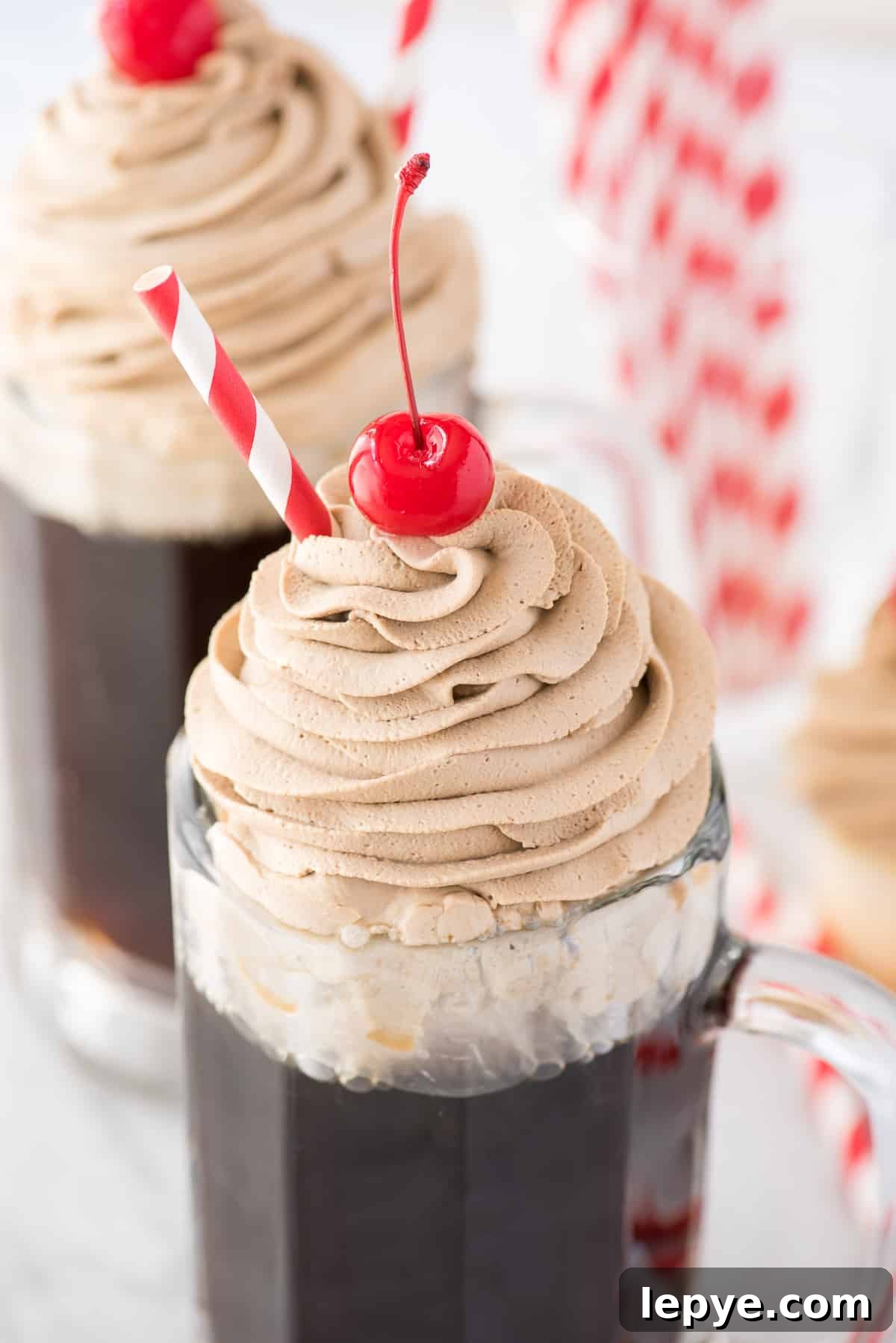 root beer whipped cream piped on top of root beer in a mug with maraschino cherry and red straw