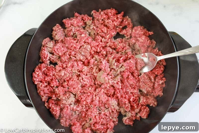 cooking ground beef in a cast iron skillet with a spoon in the skillet