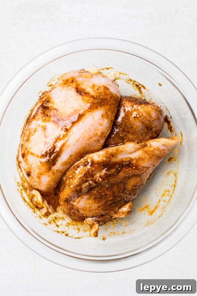 Chicken in a glass bowl shown coated with spices.