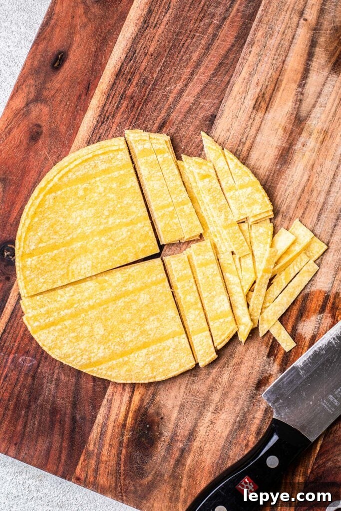 Corn tortillas on a cutting board being cut into thin strips.