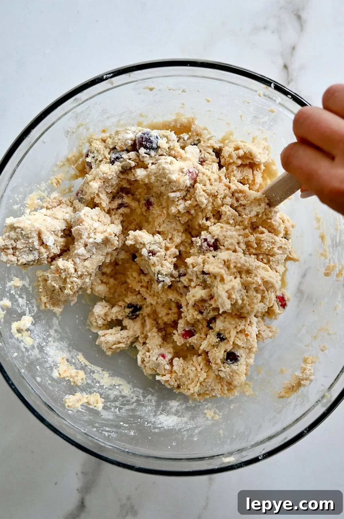 Using a spatula to gently fold all the ingredients together to make orange cranberry scones.