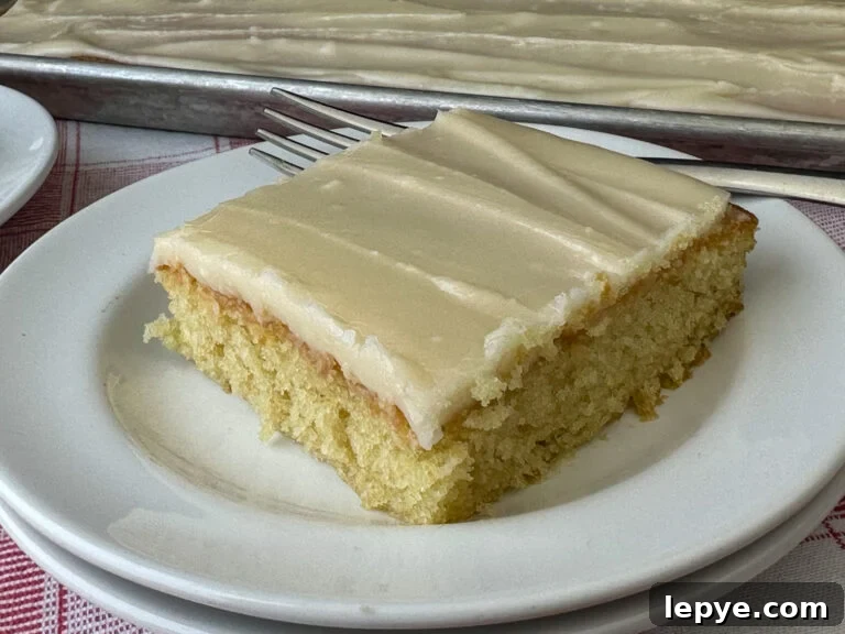 Southern-Style White Texas Sheet Cake Recipe 2 Warm buttery flavors in a square piece of Texas white sheet cake with a nice layer of homemade icing coating the top of the moist cake on a stack of white plates with a fork resting on the back and a full sheet cake in the background.