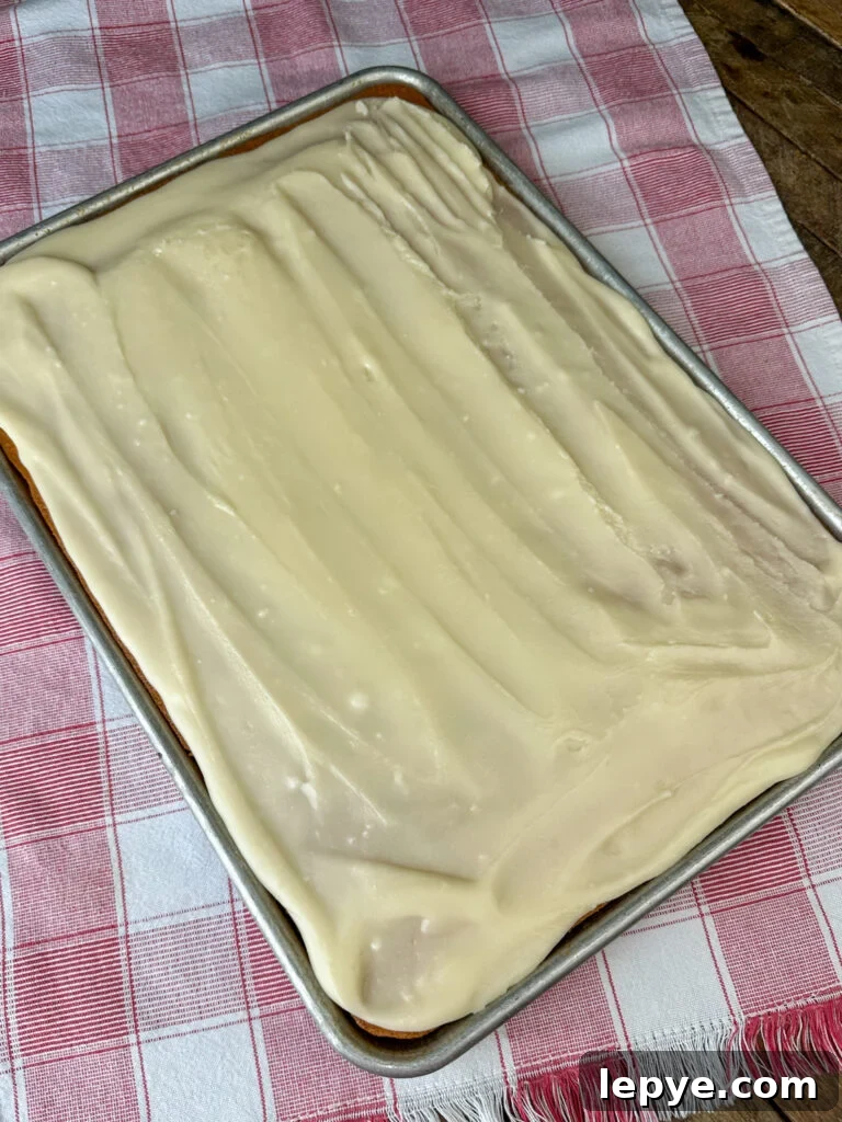 Southern-Style White Texas Sheet Cake Recipe 11 Warm frosting poured over a slightly warm 10 x 15" jelly roll pan full of all white sheet cake on a red and white napkin.