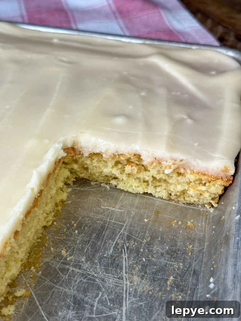 Southern-Style White Texas Sheet Cake Recipe 12 A few pieces of blonde Texas sheet cake missing from a silver jelly roll pan on a red and white napkin revealing a moist buttery cake with a cream colored vanilla icing on top.