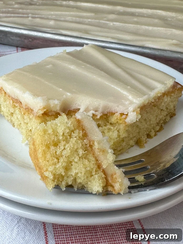 Southern-Style White Texas Sheet Cake Recipe 3 Close up of a piece of moist white Texas sheet cake on a fork next to a full piece that looks irresistible on a white plate.
