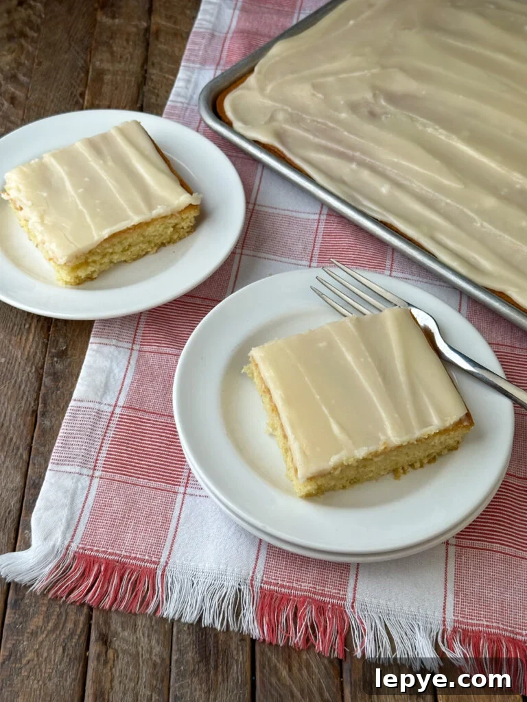 Southern-Style White Texas Sheet Cake Recipe 4 Overhead view of two pieces of homemade white Texas sheet cake on white plates resting on a red and white plaid napkin with the full sheet cake beside them.
