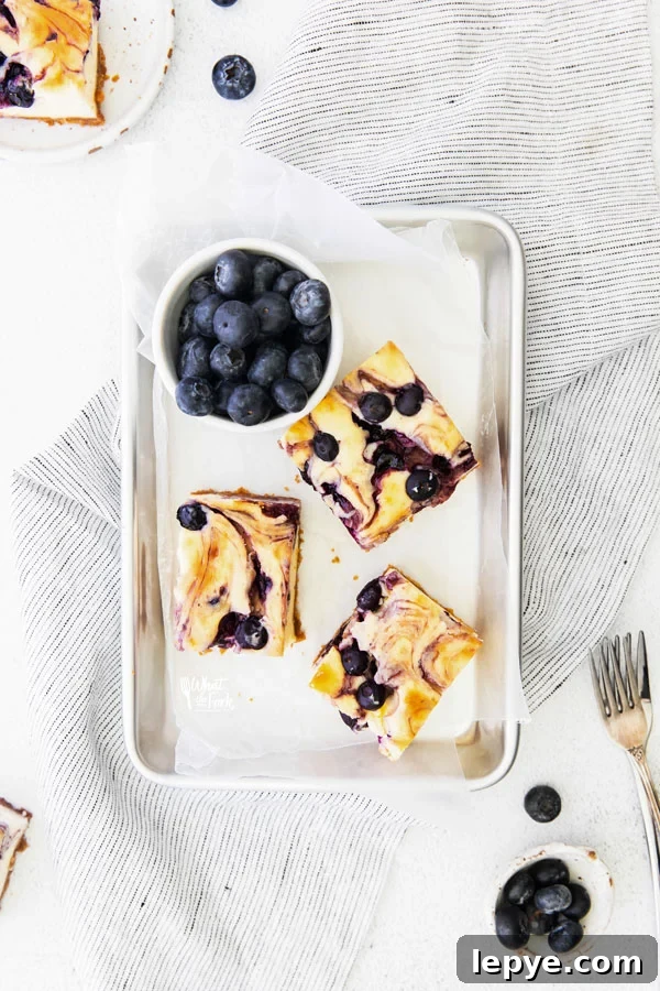 overhead shot of 3 Gluten Free Blueberry Cheesecake Bars on a parchment paper lined 1/8 sheet pan