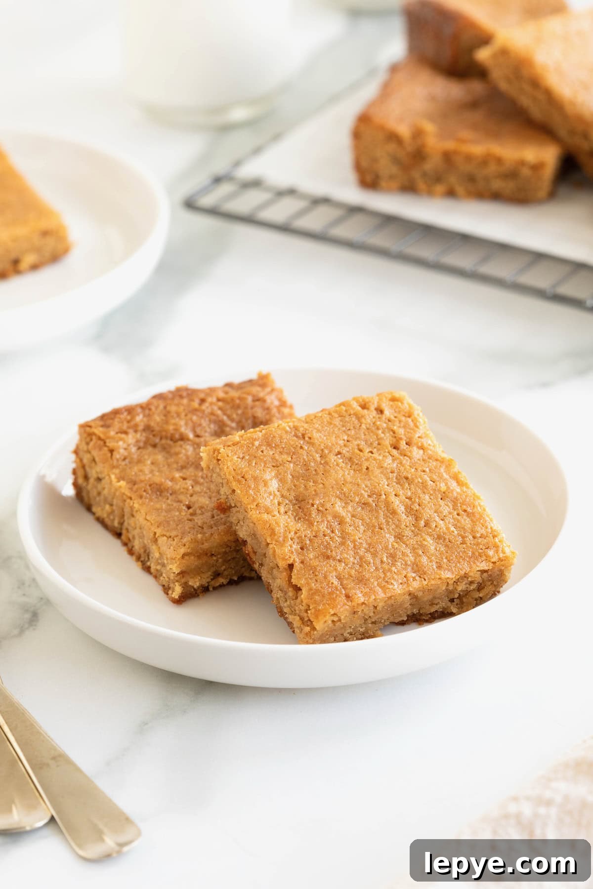 Two peanut butter brownies on a small white rimmed plate on a white marble counter.