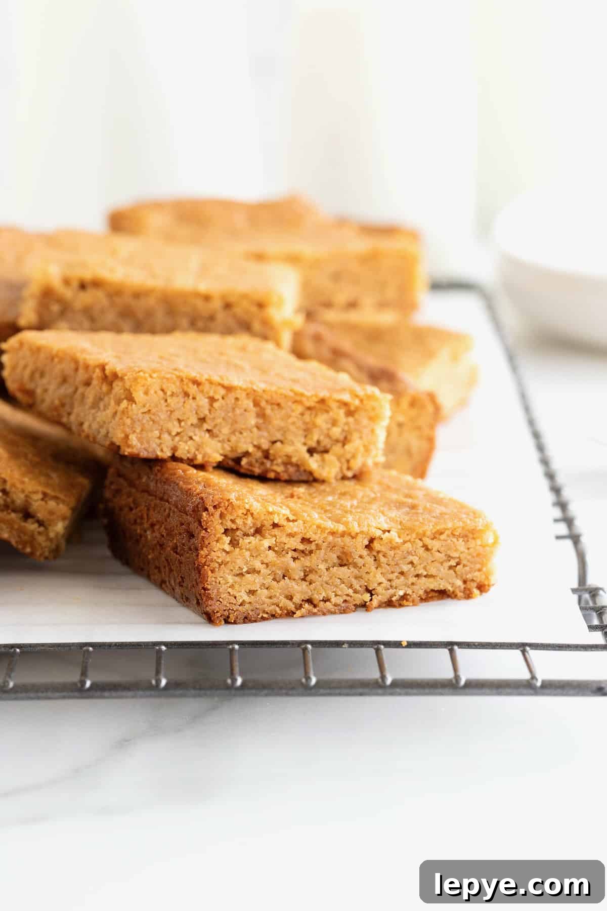 Three peanut butter blondies stacked on a parchment lined cooling rack.