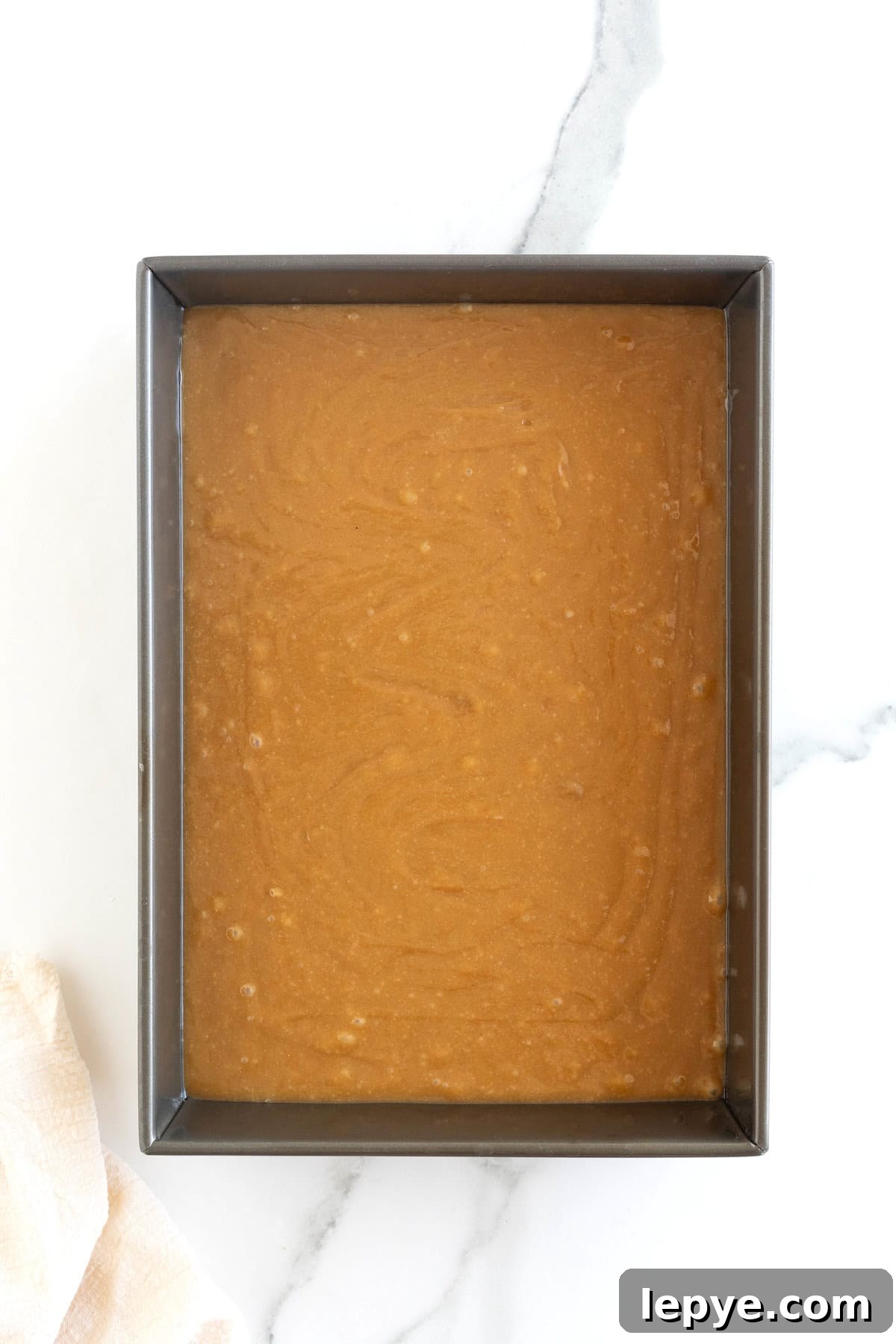 A dark aluminum baking pan of peanut butter blondie batter on a white marble counter.
