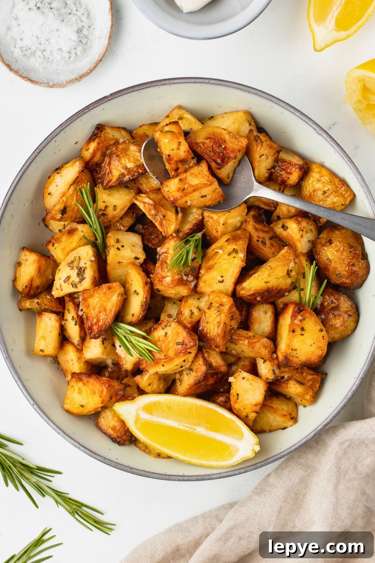 Crispy Oven-Roasted Potatoes with Garlic and Herbs 2 Sliced potatoes in a white bowl with a spoonful lifting a serving out.