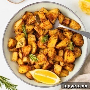 Crispy Oven-Roasted Potatoes with Garlic and Herbs 13 Sliced potatoes in a white bowl with a spoonful lifting a serving out.