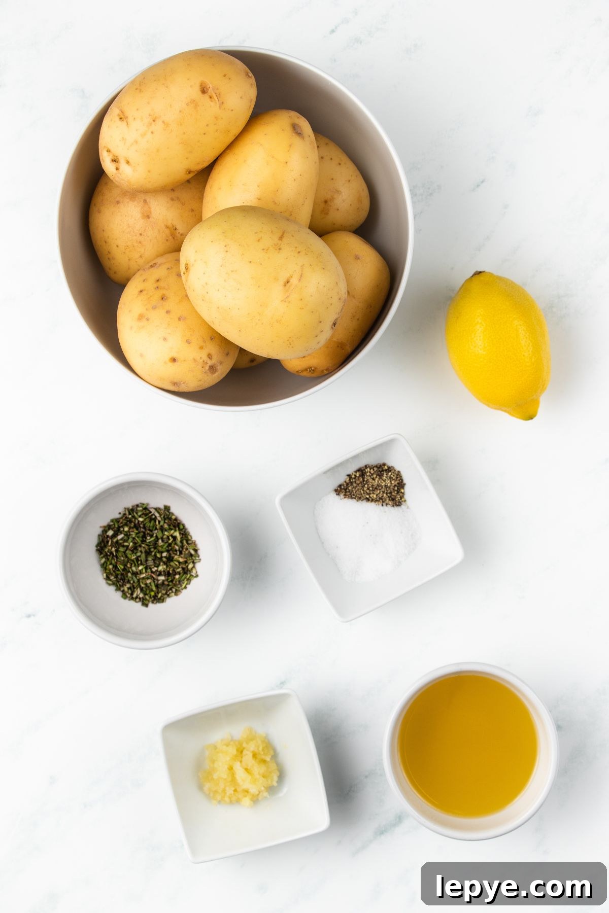 Crispy Oven-Roasted Potatoes with Garlic and Herbs 3 Ingredients needed to make roasted potatoes measured in small bowls on a white marble table.