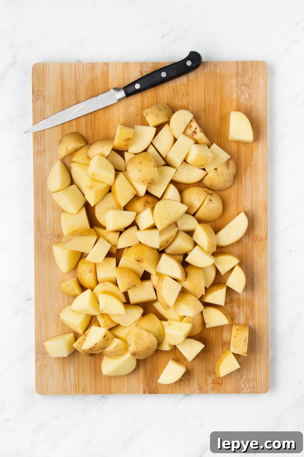 Crispy Oven-Roasted Potatoes with Garlic and Herbs 4 Potatoes cut into small pieces on a wooden cutting board.