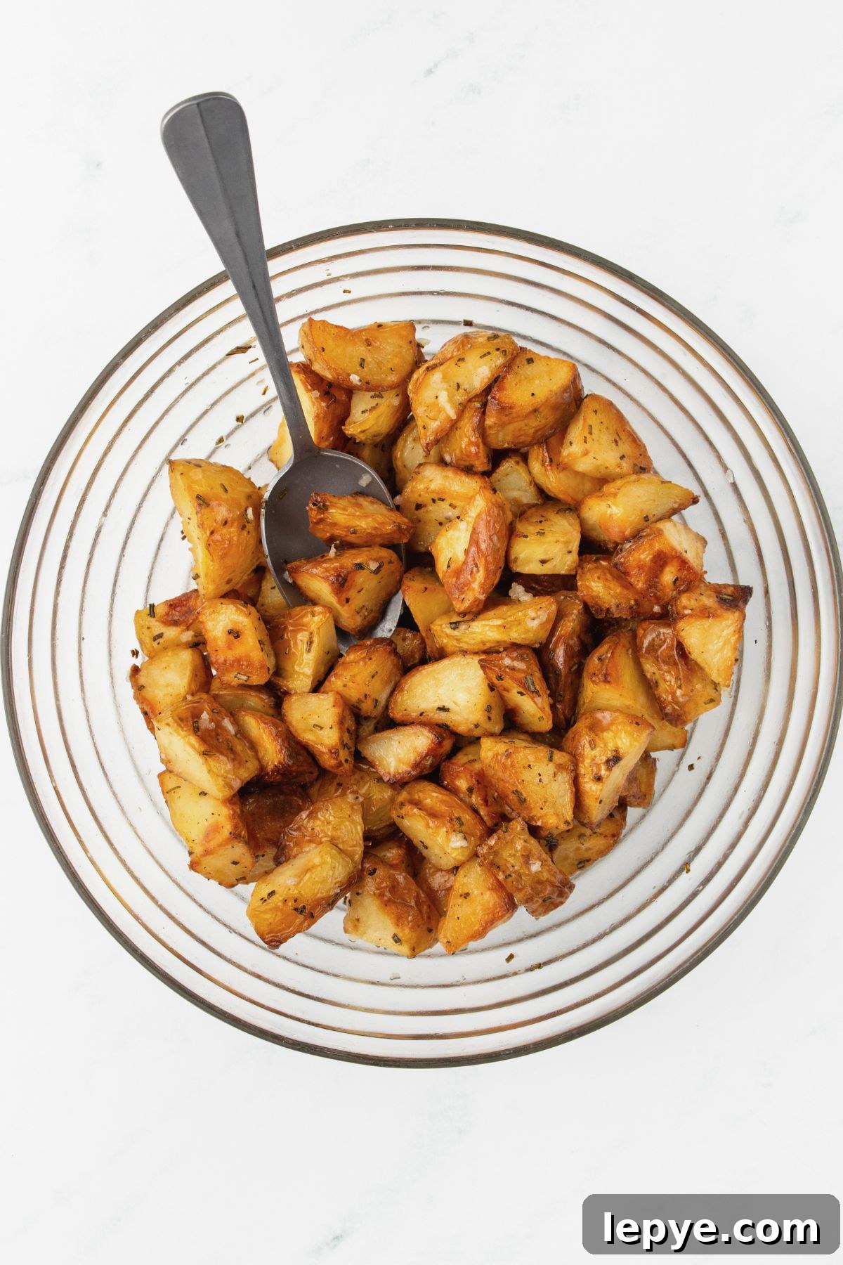 Crispy Oven-Roasted Potatoes with Garlic and Herbs 7 Pieces of potatoes being tossed with lemon juice and garlic in a large bowl.