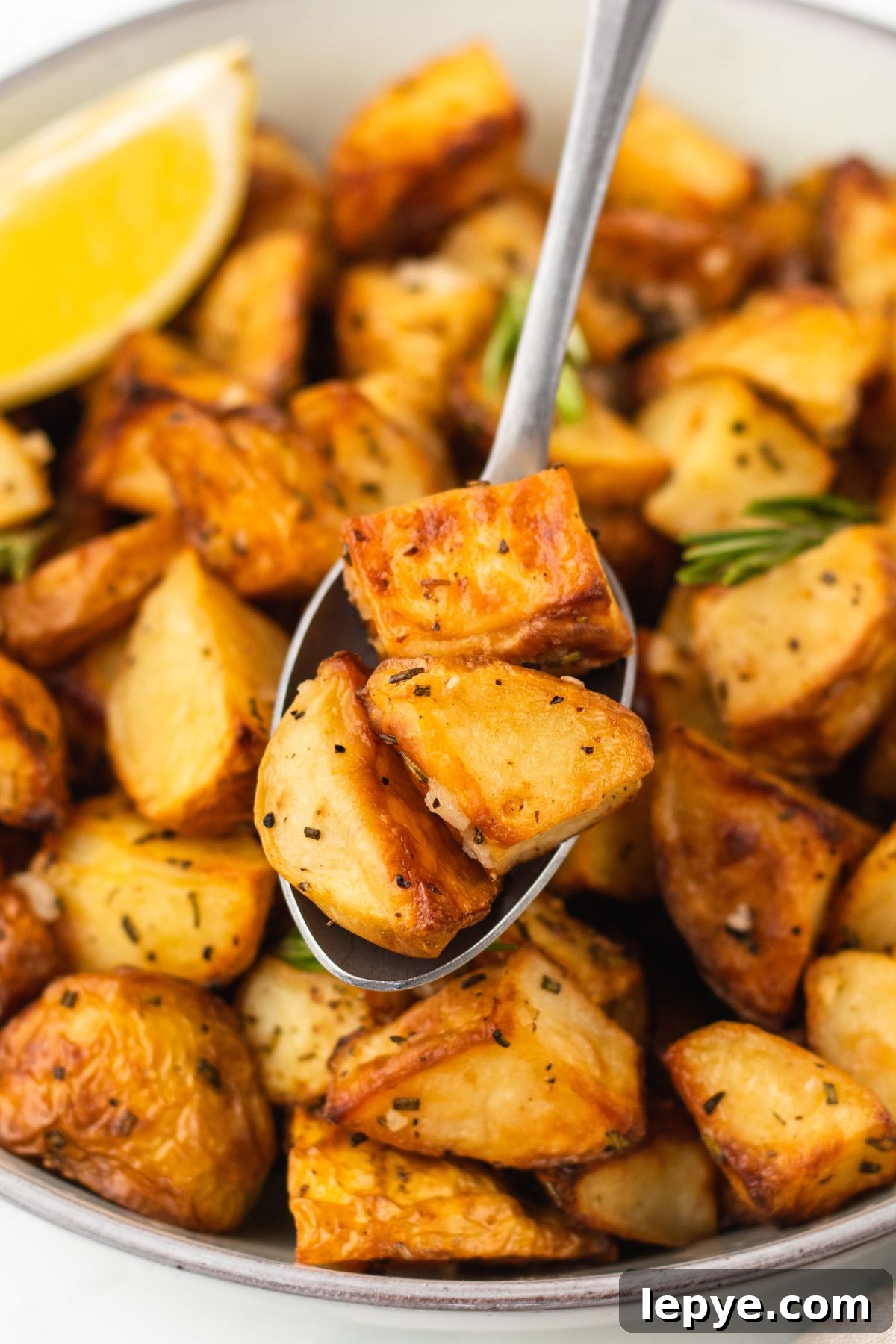 Crispy Oven-Roasted Potatoes with Garlic and Herbs 8 Easy garlic roast potatoes in a white bowl with a spoonful lifting a serving out.