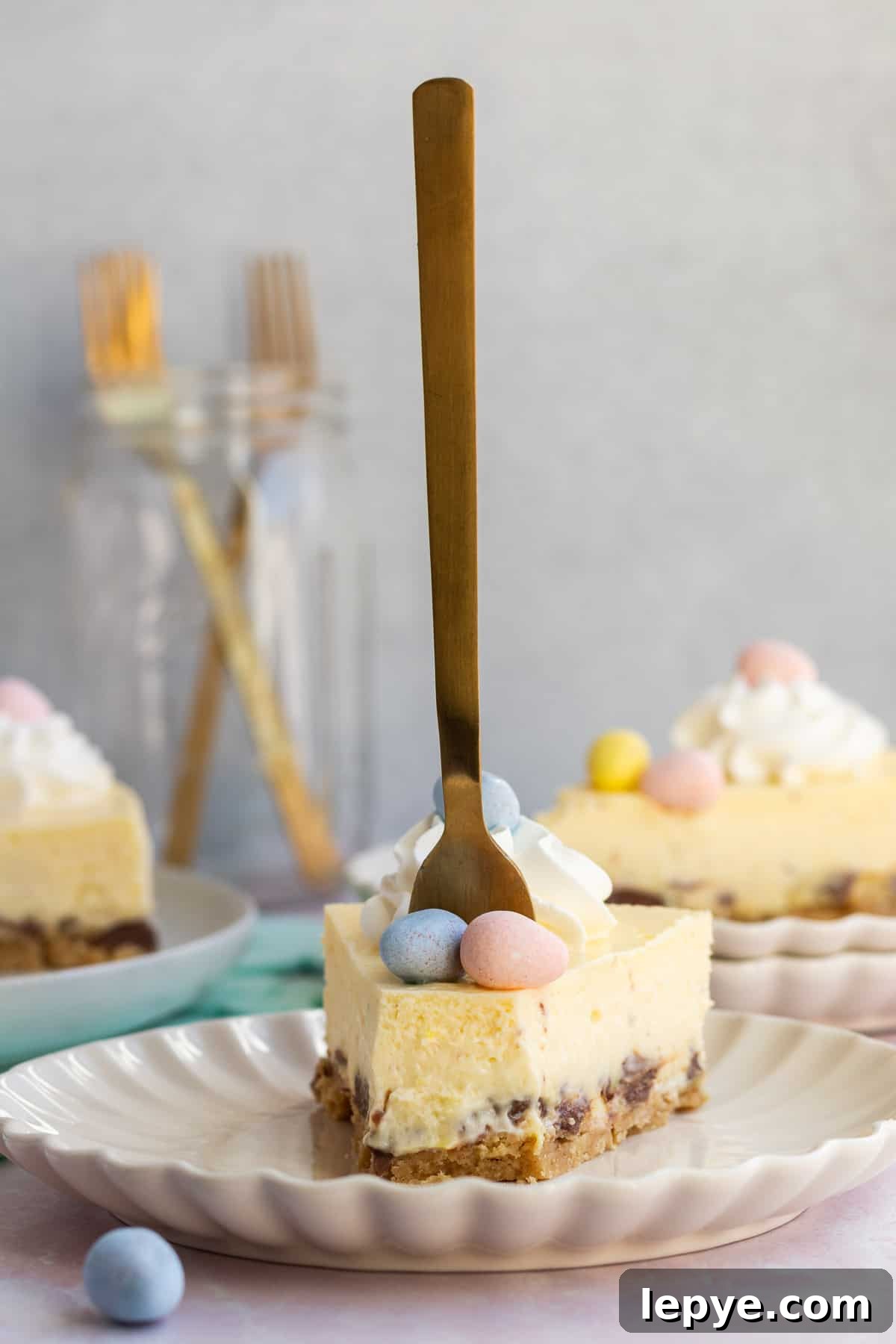 a slice of Easter egg cheesecake on a plate with a gold fork sticking up straight in it and other slices in the background