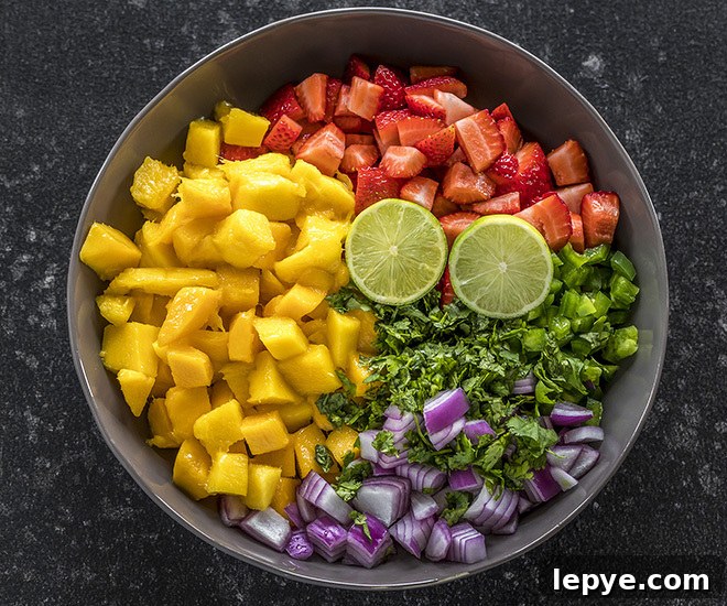 a large bowl with diced mangoes, strawberries, onion, jalapeño, cilantro and cut lime